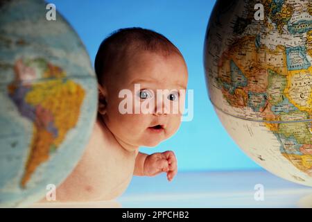 Ritratto in studio di un bambino molto curioso che strisciava tra due globi Foto Stock