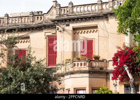 Rabat, Malta - 13 novembre 2022: Casa residenziale con persiane rosse e un arbusto di fiori rossi Foto Stock