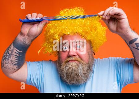 Stupito uomo divertente con tatuaggi ha un grande pettine in mano Foto Stock
