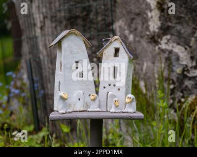 Angelsberg, Svezia - 28 maggio 2022: Un vivace giardino in primo piano, con case in ceramica e una piccola birdhouse adagiato tra le piante. Un orologio d'oca da afa Foto Stock