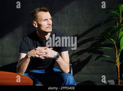 Bell'uomo attento seduto davanti alla parete nera Foto Stock