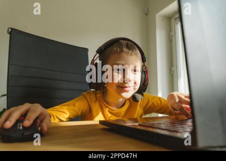 Ragazzo sorridente che indossa una cuffia per giocare ai videogiochi sul laptop Foto Stock