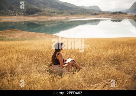 Giovane donna con sketch pad seduto di fronte al lago Rama Foto Stock