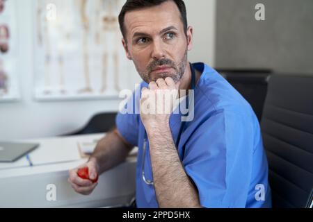 Medico premuroso con la sfera di sforzo seduta in clinica Foto Stock