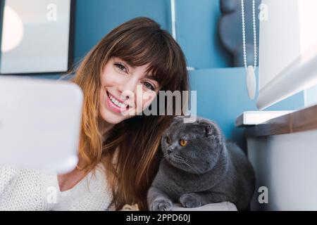 Donna felice che prende selfie con gatto a casa Foto Stock