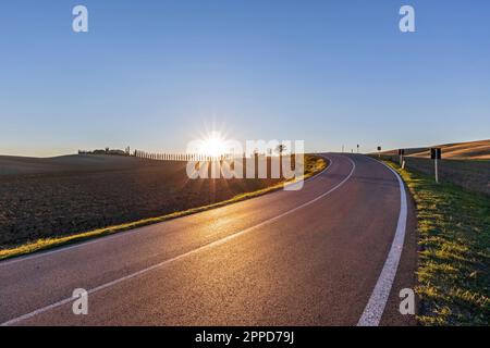 Italia, Toscana, Castiglione d'Orcia, Sole che sorge su strada asfaltata che attraversa la Val d'Orcia Foto Stock