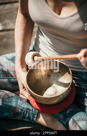 Donna seduta a zampe incrociate con ciotola di canto tibetana Foto Stock