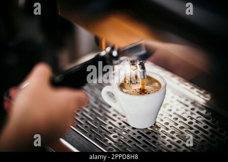 Getto di espresso che gocciola nella tazza attraverso la macchina per il caffè Foto Stock