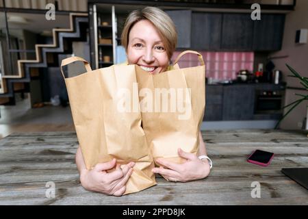 Donna felice con sacchetti di carta sul tavolo a casa Foto Stock