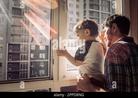 Padre e figlio che guardano fuori dalla finestra a casa Foto Stock