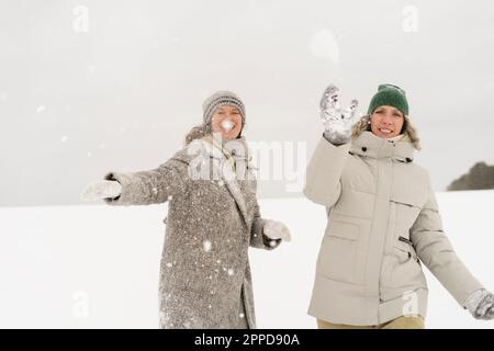 Donne felici che si divertano a lanciare la palla di neve in inverno Foto Stock