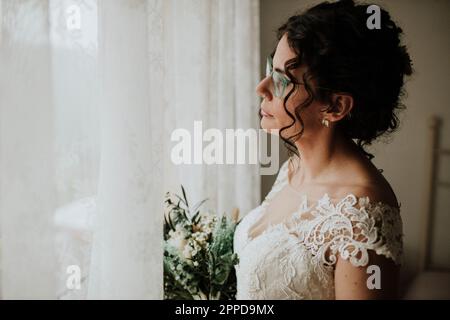 Sposa premurosa con bouquet che guarda fuori dalla finestra Foto Stock