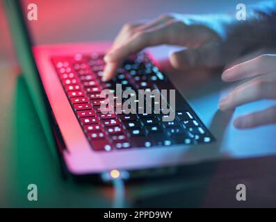 Hacker che lavora su un computer portatile illuminato in ufficio Foto Stock