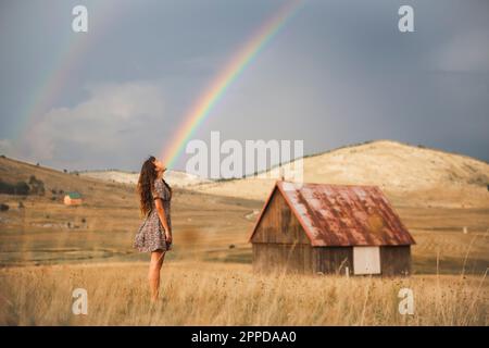 Giovane donna che guarda l'arcobaleno in piedi nel prato Foto Stock