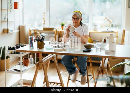 Donna anziana pittura stoviglie in officina Foto Stock
