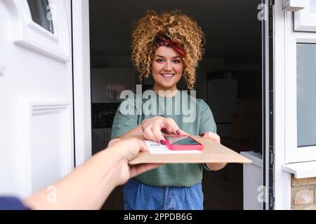 Donna felice con smartphone che prende la consegna del pacchetto Foto Stock