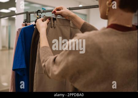Il proprietario del negozio appende gli abiti sulla rastrelliera in negozio Foto Stock