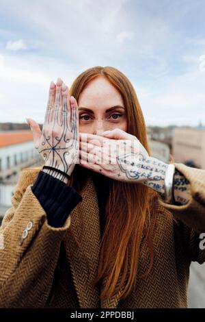 Donna con la mano tatuata che copre il viso Foto Stock