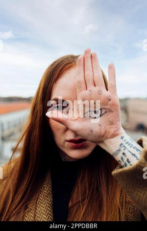 Donna che mostra occhio tatuaggio a portata di mano in terrazza Foto Stock