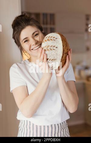 Felice giovane donna in piedi con pane appena sfornato a casa Foto Stock