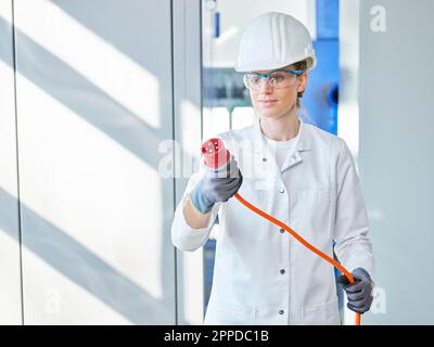 Donna che indossa un camice da laboratorio che esamina la spina di alimentazione in laboratorio Foto Stock