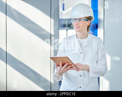 Donna che indossa un camice da laboratorio con un tablet PC in laboratorio Foto Stock