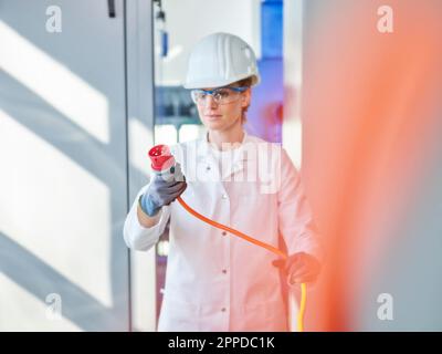 Donna che indossa un camice da laboratorio per l'analisi della spina di alimentazione in laboratorio Foto Stock