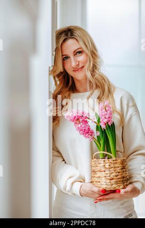 Donna sorridente che tiene fiori rosa appoggiati al muro Foto Stock