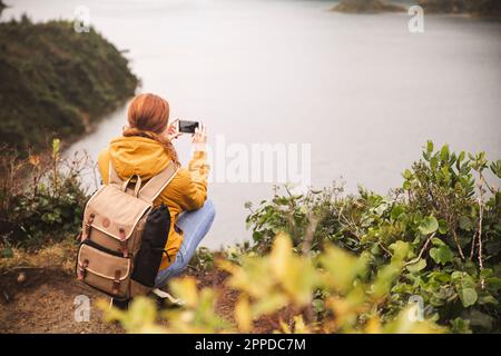 Giovane donna che fotografa il lago con uno smartphone Foto Stock