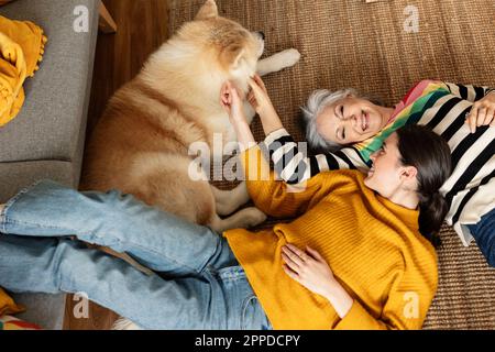 Felice madre e figlia accarezzando il cane sdraiato sul tappeto a casa Foto Stock
