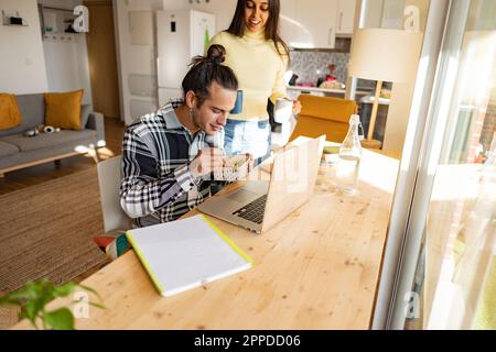 Freelance che mangia uno spuntino e che ha un caffè in ufficio a casa Foto Stock
