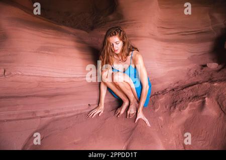 Giovane donna accovacciata sulla roccia rossa nella grotta Foto Stock