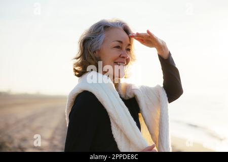 Donna matura felice che scherza gli occhi in piedi alla spiaggia Foto Stock