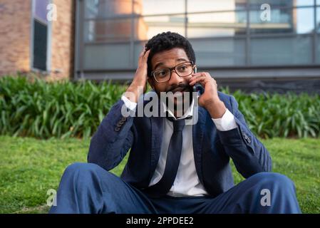 Scioccato uomo d'affari che parla su smartphone fuori ufficio edificio Foto Stock