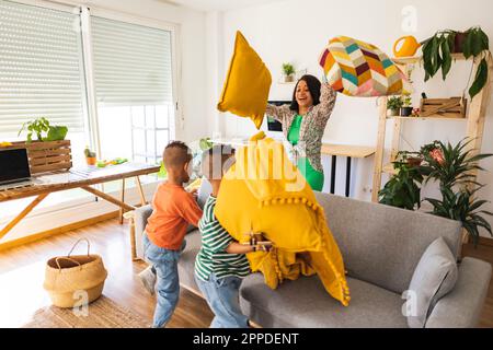 Giocosa madre che gioca a cuscino lotta con i figli gemelli a casa Foto Stock