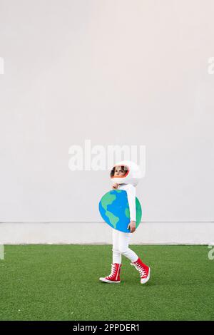 Ragazza vestita come astronauta camminare sull'erba tenendo la terra tagliata fuori Foto Stock