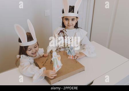 Sorelle che indossano orecchie di coniglio facendo decorazioni per Pasqua a casa Foto Stock