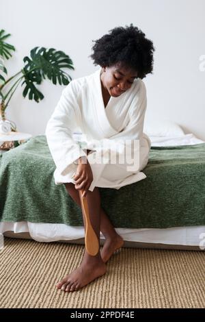 Donna che massaggia la gamba con la spazzola in camera da letto a casa Foto Stock