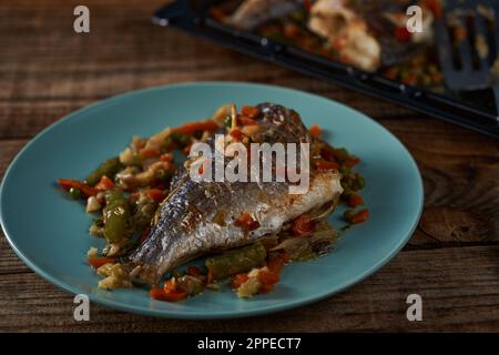 Orata alla griglia con verdure su un piatto blu su un asse di legno Foto Stock