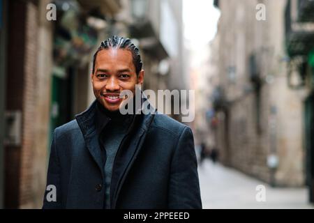 Elegante uomo afroamericano che guarda la macchina fotografica e sorridente mentre si posa in piedi all'aperto. Foto Stock