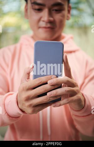 Giovane uomo con felpa con cappuccio rosa che prende selfie su smartphone per il suo account di social media Foto Stock