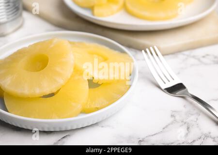 Gustose fette di ananas in scatola e forchetta su un tavolo di marmo bianco Foto Stock