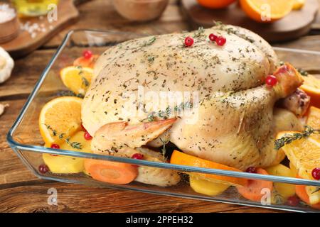 Pollo crudo, fette di arancia e altri ingredienti in teglia da forno su tavolo di legno Foto Stock