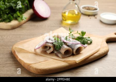 Tavola di legno con deliziosi filetti di aringhe salate, anelli di cipolla e prezzemolo Foto Stock