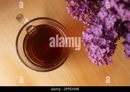 Bellissimi fiori di lilla e una tazza di tè in vetro su un tavolo di legno, vista dall'alto Foto Stock