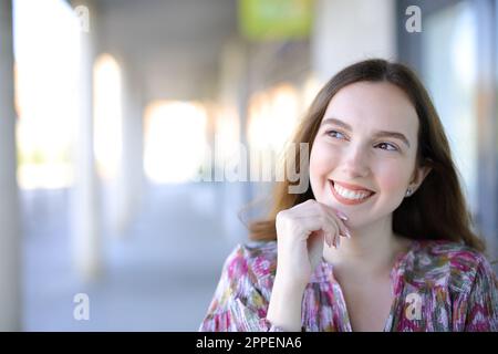 Donna felice che pensa guardando lateralmente per strada Foto Stock