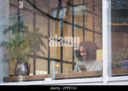 Giovane donna che usa il telefono delle cellule nel caffè Foto Stock