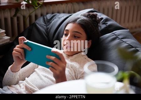 Ragazza sdraiata sul sacchetto del fagiolo e che gioca i video giochi Foto Stock