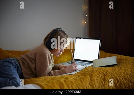 Ragazza che fa i compiti con il laptop nella sua camera da letto Foto Stock