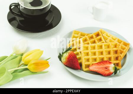 Tulipani freschi e waffle alla frutta belgi, vista dall'alto. Colazione gustosa. Colazione per una persona cara. Waffle fatti in casa su un piatto. Sfondo con spazio di copia Foto Stock